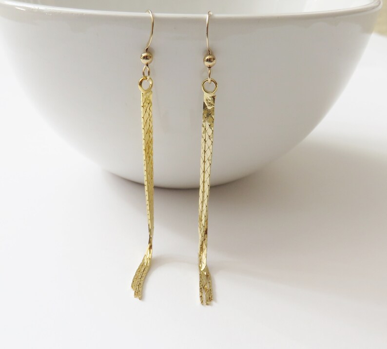 May include: A pair of gold-tone dangle earrings with a chain link design. The earrings are long and slender, and they have a simple, elegant look.