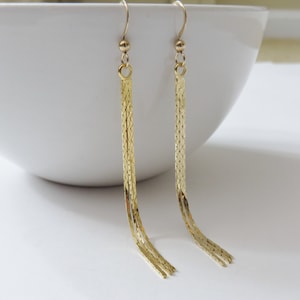 May include: A pair of gold dangle earrings with a chain link design. The earrings are long and have a tassel-like appearance.