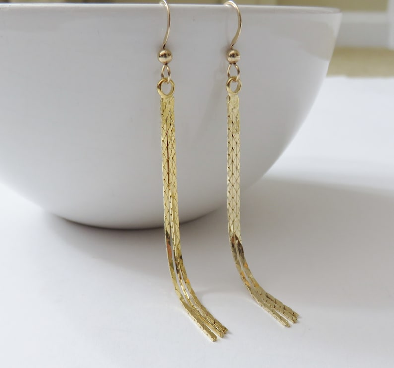 May include: A pair of gold dangle earrings with a chain link design. The earrings are long and have a tassel-like appearance.