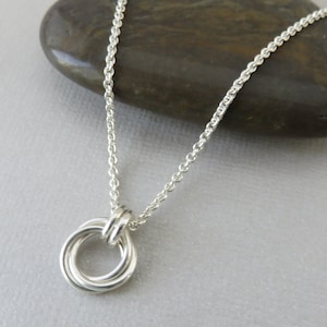 May include: A silver chain necklace with a silver circle pendant made of three intertwined rings.