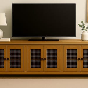 May include: A light brown wooden TV stand with six cabinet doors, each featuring a dark mesh panel. A black television sits on top. A white lamp and vase with greenery are on the stand.