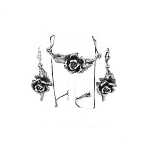 Puede incluir: Un conjunto de collar y pendientes de plata con un diseño de rosa. El collar tiene una cadena delicada y un colgante con una sola rosa. Los pendientes son pendientes colgantes con una sola rosa cada uno.