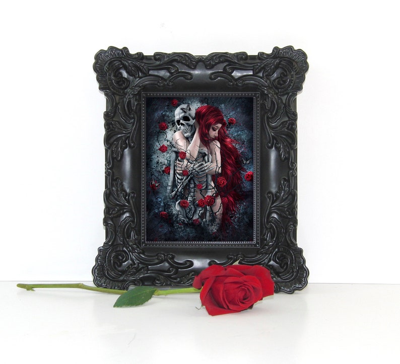 Op de afbeelding: Een ingelijste gotische kunstprint met een vrouw met lang rood haar die een skelet omarmt. De achtergrond is een donker, getextureerd oppervlak met rode rozen.
