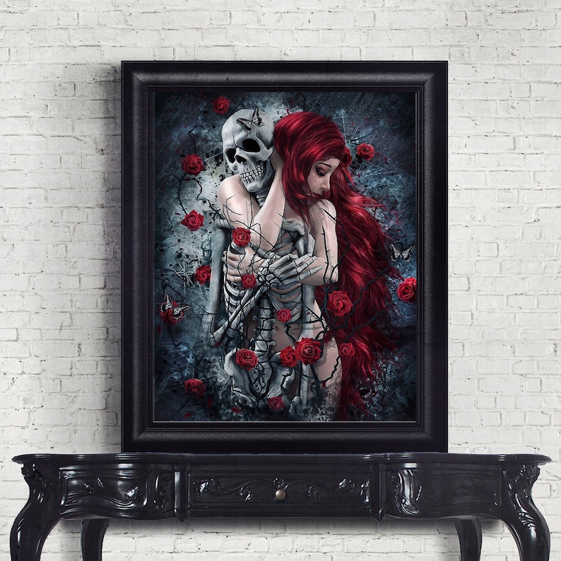 Op de afbeelding: Een ingelijst gotische kunstprint met een vrouw met lang rood haar die een skelet omarmt. De achtergrond is donkerblauw met rode rozen en vlinders.