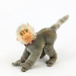 May include: A grey and white plush monkey toy with green eyes and a red collar. The monkey is sitting on a white background.