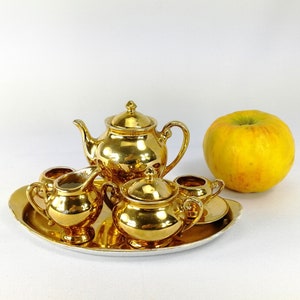 May include: A gold tea set with a teapot, creamer, sugar bowl, and two cups on a gold tray. The set is on a white background.