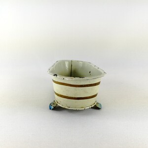 May include: A white enamel bathtub with gold stripes and blue feet. The bathtub is a miniature toy.