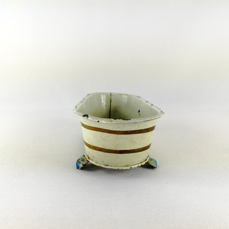 May include: A white enamel bathtub with gold stripes and blue feet. The bathtub is a miniature toy.