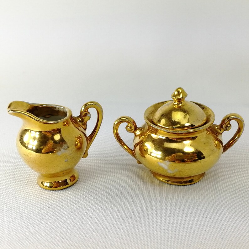 May include: A gold-plated porcelain creamer and sugar bowl set. The creamer has a handle and a spout. The sugar bowl has a lid and two handles.