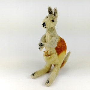 Könnte beinhalten: Ein Plüschtier-Känguru mit einem Joey in seiner Tasche. Das Känguru ist hellbraun und weiß mit schwarzen Augen und einer schwarzen Nase. Der Joey ist eine kleinere Version des Kängurus und ist hellbraun.