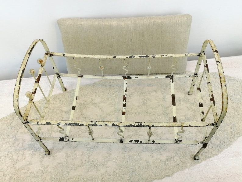 K&ouml;nnte beinhalten: Ein wei&szlig;es Metall-Puppenbettgestell mit einer wei&szlig;en Stoffmatratze. Das Bettgestell hat ein schlichtes Design mit abgerundeten Kanten und einigen dekorativen Details.