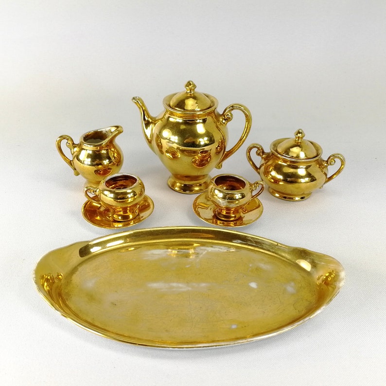 May include: A gold-plated tea set with a teapot, creamer, sugar bowl, and two cups and saucers. The set is displayed on a gold-plated serving tray.
