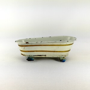May include: White enamel bathtub with gold stripes and blue feet. The bathtub is a vintage toy.