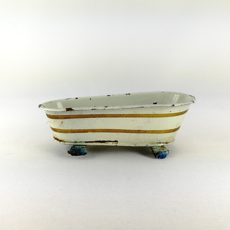 May include: White enamel bathtub with gold stripes and blue feet. The bathtub is a vintage toy.