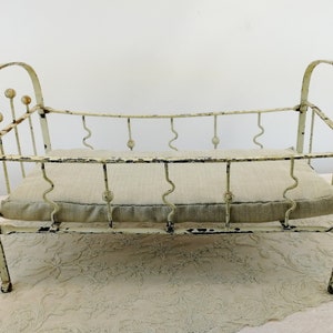K&ouml;nnte beinhalten: Ein wei&szlig;es Puppenbett aus Metall mit einer wei&szlig;en Stoffmatratze. Das Bett hat ein schlichtes Design mit abgerundeten Kanten und dekorativen Kugeln am Kopfende.