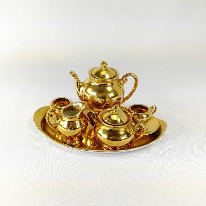 May include: A gold-toned tea set with a teapot, creamer, sugar bowl, and two cups on a gold-toned tray.