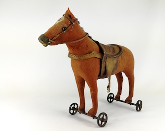 May include: A brown plush toy horse with a saddle and bridle, on wheels. The horse has a white patch on its forehead and black eyes.