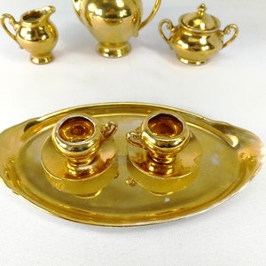 May include: A gold-colored tea set with a tray, teapot, creamer, sugar bowl, and two cups. The set is made of porcelain and has a shiny, metallic finish.