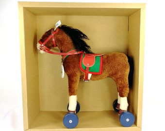 May include: A brown plush toy horse with a red saddle and green trim, on wheels, in a cardboard box.