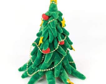 May include: A plush green Christmas tree toy featuring soft fabric branches, decorated with small yellow felt stars and red felt ornaments. A larger yellow star sits at the top, and a thin gold string with star accents is draped around.