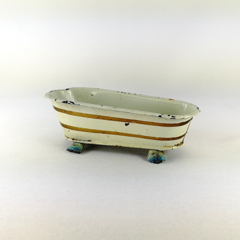 May include: A white metal bathtub with gold stripes and blue feet. The bathtub is a toy.