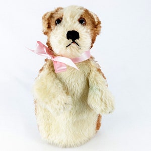 May include: A plush brown and white dog puppet with a pink bow tie. The puppet has a white face with brown eyes and a black nose.