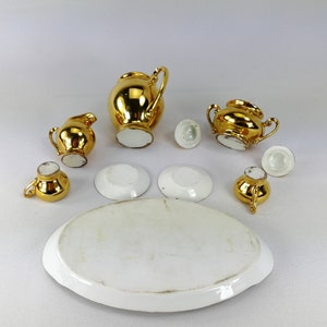 May include: A miniature gold tea set with a teapot, creamer, sugar bowl, and four saucers. The set is made of porcelain with gold accents.