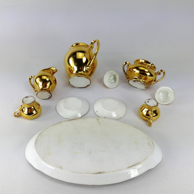 May include: A miniature gold tea set with a teapot, creamer, sugar bowl, and four saucers. The set is made of porcelain with gold accents.