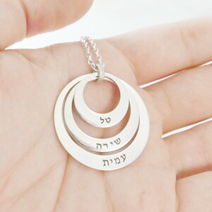 May include: Silver necklace with three concentric circles, each inscribed with a Hebrew word: 'עמות', 'שירה', and 'סלי'.