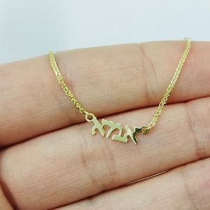 May include: A gold chain necklace with a pendant featuring the Hebrew word "Chai" which means "life" in English.