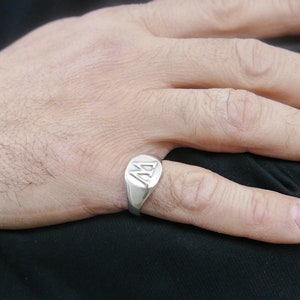 Op de afbeelding: Een zilveren zegelring met een verhoogde letter 'A' op de voorkant.