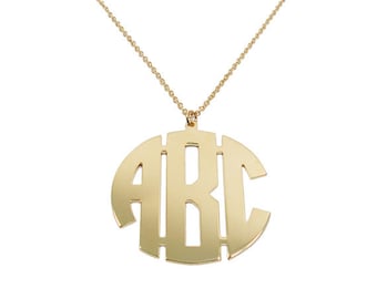 Puede incluir: Un collar de oro con un gran colgante redondo con las letras "ABC" en estilo monograma.