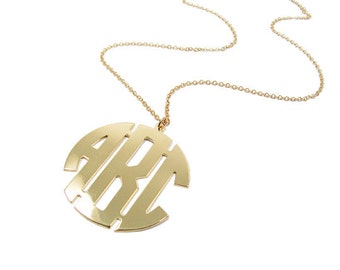 Puede incluir: Un collar de oro con un gran colgante redondo con las letras "ARI" en estilo monograma.