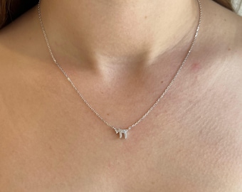 May include: A delicate silver necklace featuring a small pendant with a sparkling, gem-studded design. The necklace is displayed against a neutral background, highlighting the pendant's intricate details and the chain's subtle shine. The necklace is a piece of jewelry.