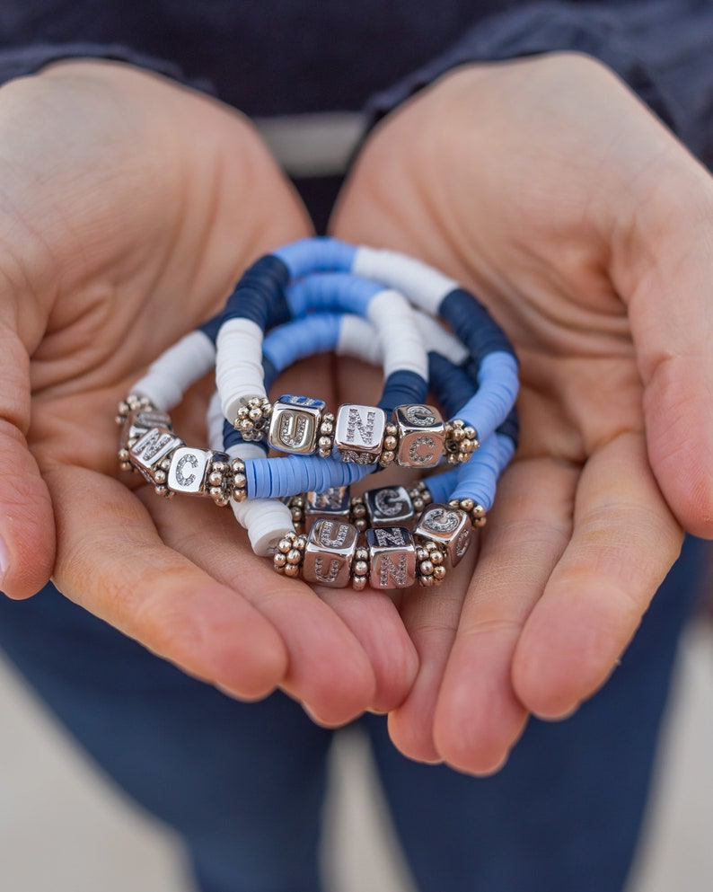 May include: A set of three bracelets with blue and white beads and silver charms with letters on them.