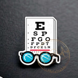 May include: A 1.5-inch acrylic pin featuring a white eye chart with the letters E, SP, FGO, FPDT, and DFCLEN. Below the chart are blue-lensed glasses. The pin has the text "1.5" Acrylic Pin".