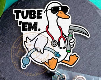 May include: A white badge reel featuring a cartoon goose wearing sunglasses, a stethoscope, and holding a medical tool. The text "TUBE 'EM" is above the goose. The reel has a clear plastic strap and a metal snap.