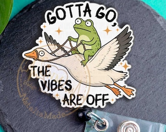 May include: A badge reel featuring a white goose flying with a green frog riding on its back. The text "GOTTA GO, THE VIBES ARE OFF" is printed in black around the illustration. The badge reel has a clear plastic strap and a metal button.