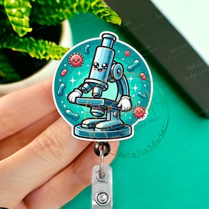 May include: A blue cartoon microscope with a smiling face and googly eyes. The microscope is surrounded by colorful bacteria and viruses. The image is printed on a round badge reel.