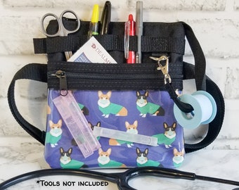 May include: Black nylon medical organizer bag with a clear front panel featuring a pattern of corgis wearing face masks and sweaters. The bag has multiple pockets, a zipper closure, and a shoulder strap. Includes scissors, pens, and tape.