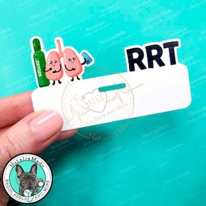 May include: A white badge reel with the letters "RRT" in black. The reel features cartoon lungs, an oxygen tank, and a small blue item. The badge reel is held by a hand, with a logo of a dog and stethoscope.