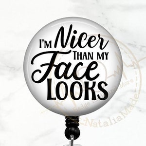 May include: A white round badge reel with a black and white design. The design says "I'm Nicer Than My Face Looks".