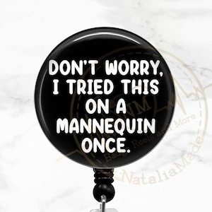 May include: Black and white badge reel with a black button and a clear plastic clip. The button has white text that reads "Don't worry, I tried this on a mannequin once."
