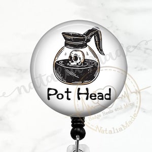 May include: A white round badge reel with a black and white illustration of a coffee pot with a skull inside. The text "Pot Head" is printed in black below the illustration.
