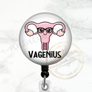 May include: A white badge reel with a clear plastic clip. The badge holder features a cartoon illustration of a uterus with a face, wearing glasses and the text "VAGENIUS".