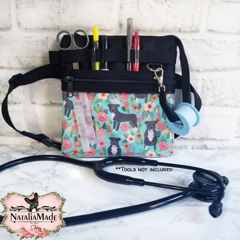 May include: A black medical fanny pack with a teal floral print featuring dog illustrations. The pack has multiple pockets holding scissors, pens, and other medical supplies. A stethoscope and tape are also visible. The text "**TOOLS NOT INCLUDED**" is displayed.