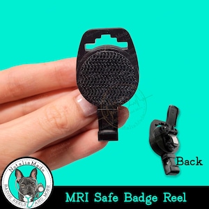 May include: Black MRI safe badge reel with a textured, circular front. The reel has a rectangular clip and a slot for attaching a badge. The words "MRI Safe Badge Reel" are at the bottom.