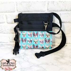May include: Black crossbody bag with a teal front panel featuring a repeating pattern of French bulldogs wearing glasses. The bag has a black adjustable strap, a zippered main compartment, and a silver clasp.