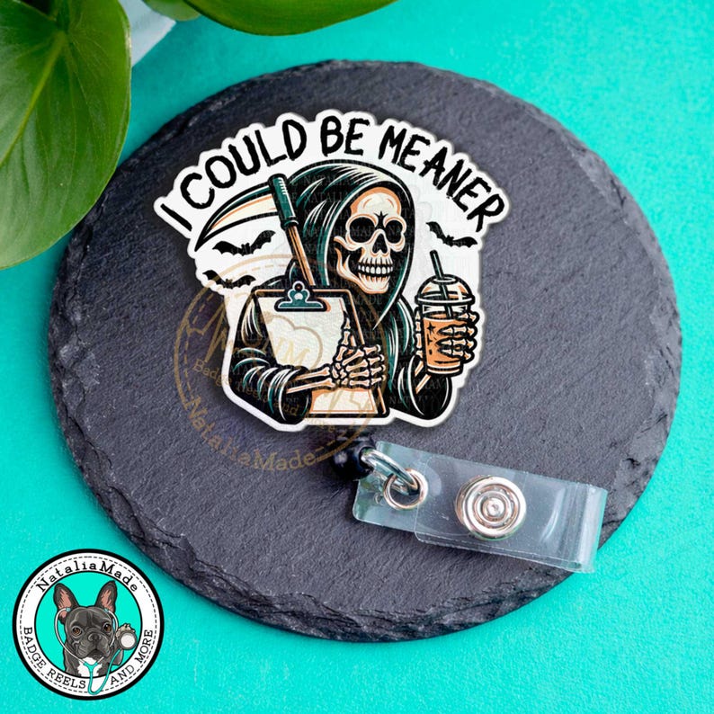 May include: A badge reel with a cartoon grim reaper holding a clipboard and a drink, with the text "I COULD BE MEANER". The reel is on a black slate-like surface with a badge reel clip.