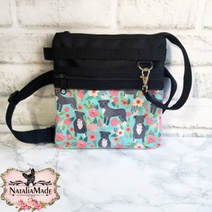 May include: Black and turquoise dog treat bag with a floral and dog pattern. The bag has a black strap and zipper closure. The bag has a silver clasp and the text "NataliaMade" on the bottom.